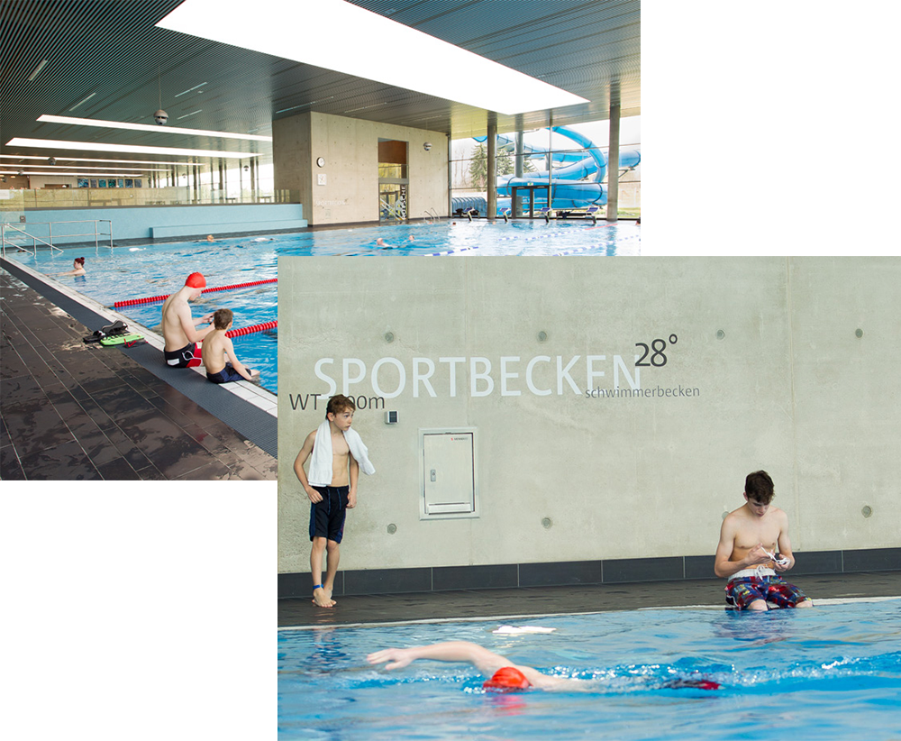Sportbecken der Sportwelt mit Schwimmern, moderner Hallenarchitektur und Blick auf die Wasserrutsche  Schwimmtraining im Sportbecken der Sportwelt mit Bahnleinen, Startbereich und Beschriftung an der Betonwand